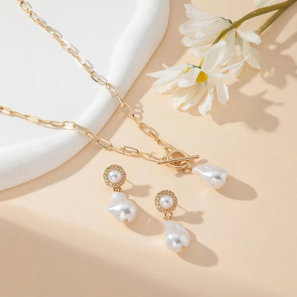 Gold-coloured retro baroque pearl pendant necklace and matching stud earrings set on a dark background.