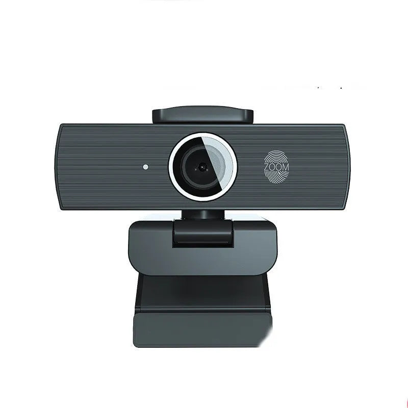 Black USB webcam with magnetic privacy cover on desk next to computer monitor