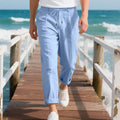 Men's straight leg linen trousers in light khaki colour with drawstring waist, laid flat.