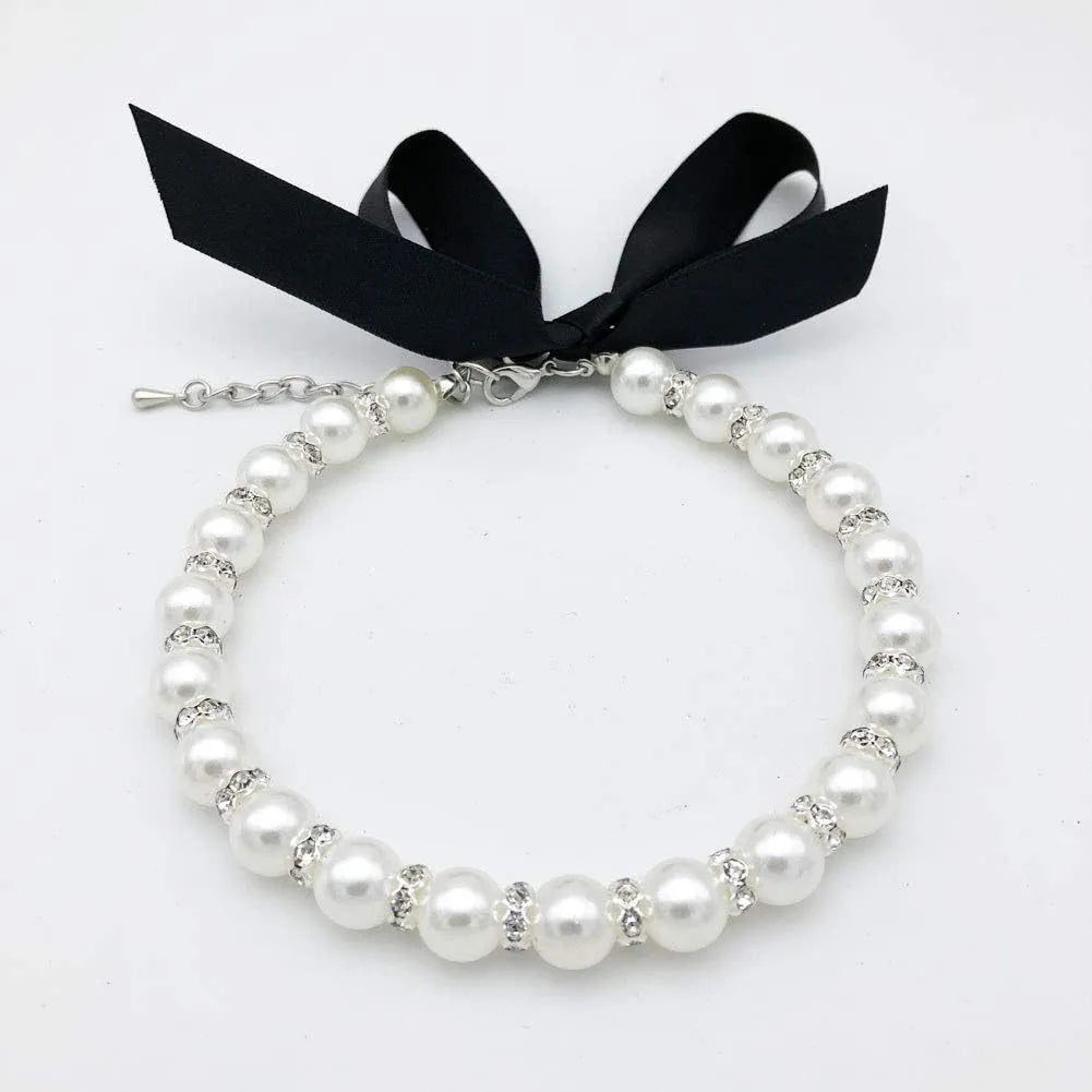 Small dog wearing adjustable blue imitation pearl and rhinestone necklace with ribbon bow