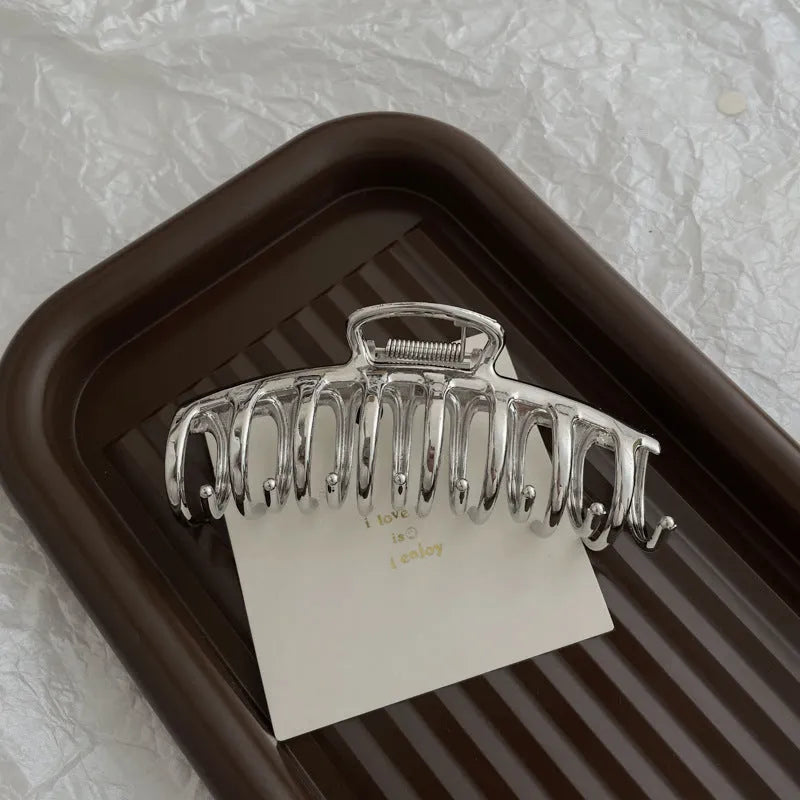 Silver metal hair claw clip assortment showing bows, waves, pearl designs, and geometric shapes from 4cm to 13.5cm