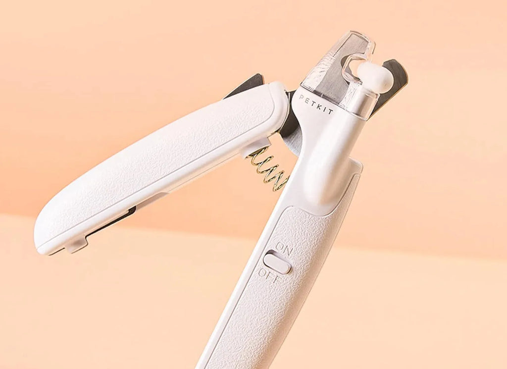 White pet nail clippers with LED light, anti-splash guard, and built-in file on a grey surface