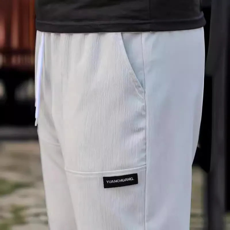 Men's straight-leg lightweight polyester trousers in light grey colour, laid flat showing front design