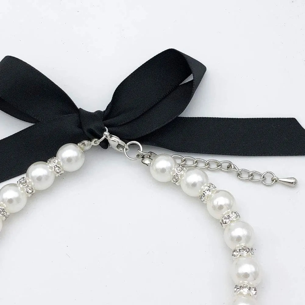 Small dog wearing adjustable blue imitation pearl and rhinestone necklace with ribbon bow