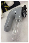 Grey handheld electric pet hair remover brush with soft rubber head, shown removing fur from upholstery.