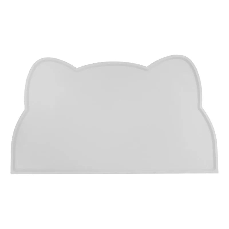 Solid colour silicone pet feeding mat in a cat head shape on a floor next to pet bowls.
