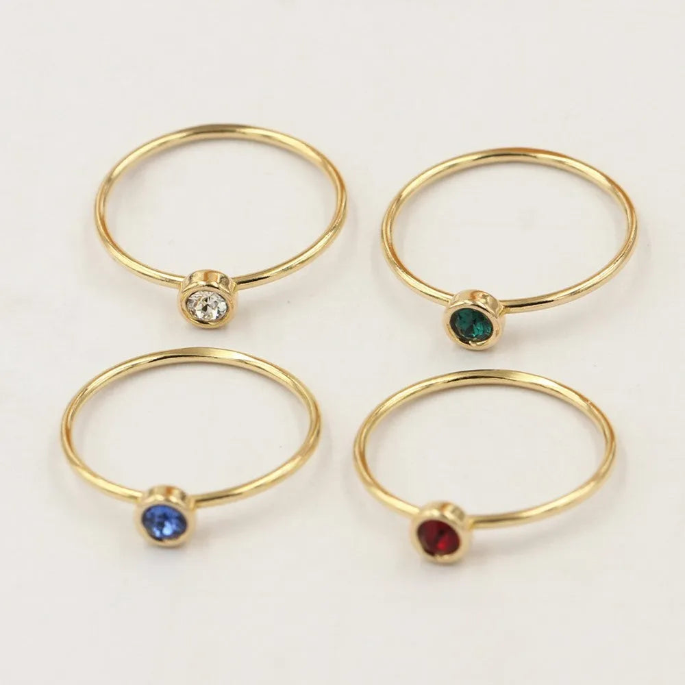 Women's 14K gilded gold-filled zircon copper knuckle ring in green, blue, dark red, or white on a finger.