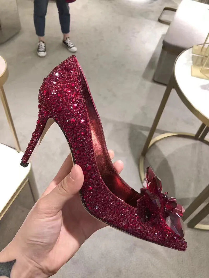 Gold women's pointed toe stiletto heels with rhinestone and bow decoration on a sequin cloth upper.