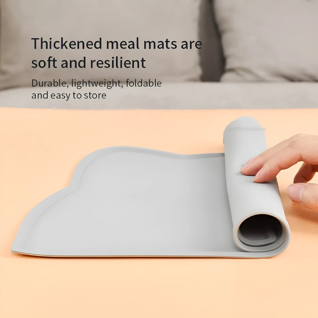 Solid colour silicone pet feeding mat in a cat head shape on a floor next to pet bowls.