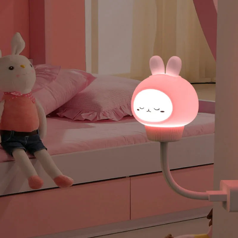 Small cartoon bear-shaped USB night light with remote control on a bedside table.