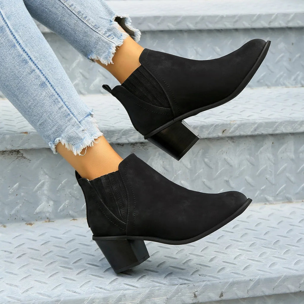 Black pointed toe ankle boots with a thick square low heel on a woman's foot.