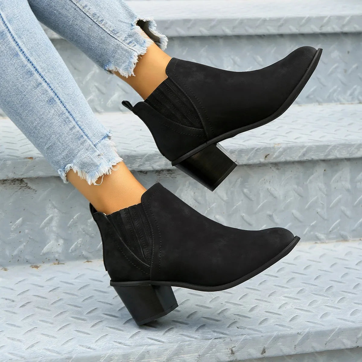 Black pointed toe ankle boots with a thick square low heel on a woman's foot.