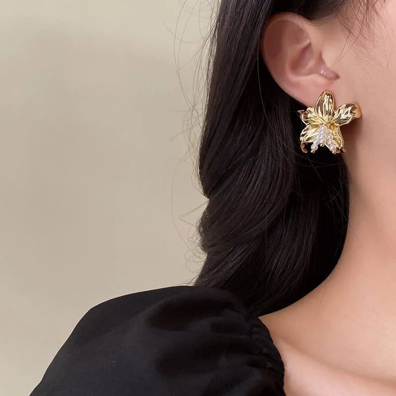 A pair of exaggerated gold metal flower earrings with pearl centres, showing a niche floral jewellery design.