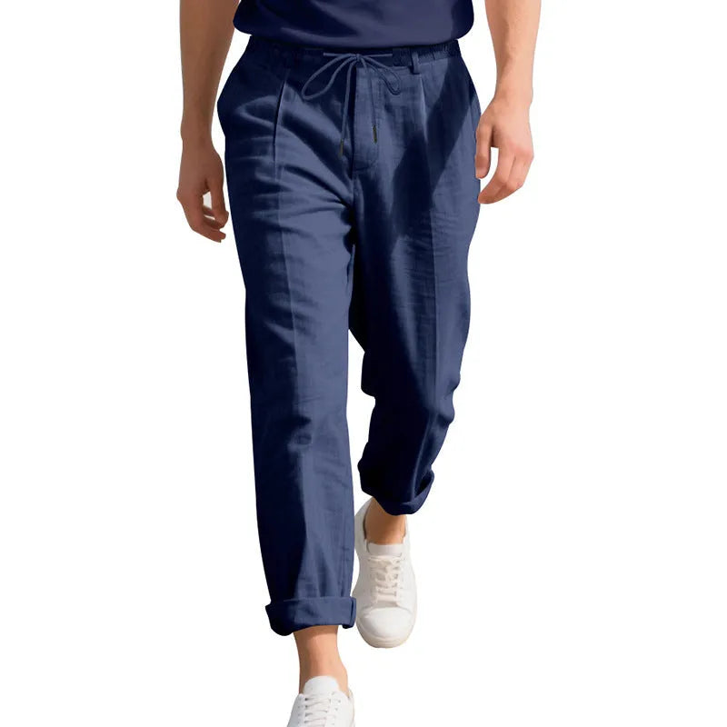 Men's straight leg linen trousers in light khaki colour with drawstring waist, laid flat.