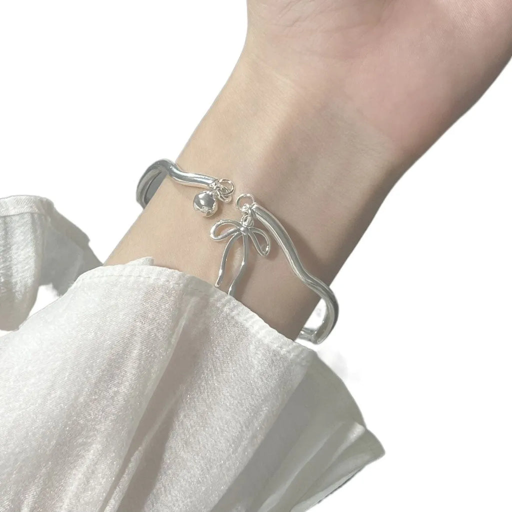 Silver adjustable bracelet with a bow charm and a visible bell-opening clasp on a white background.