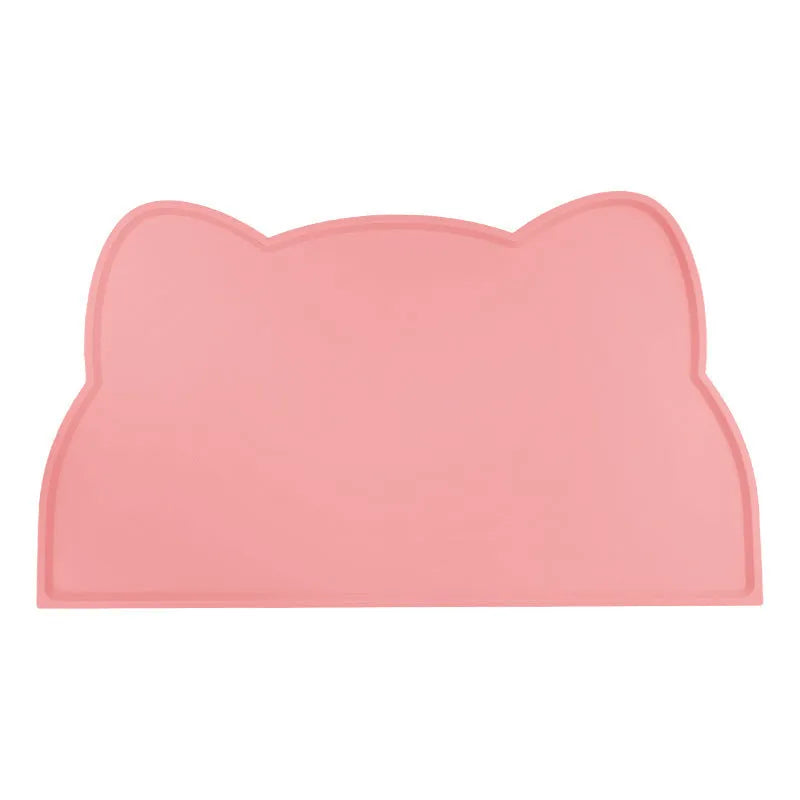 Solid colour silicone pet feeding mat in a cat head shape on a floor next to pet bowls.