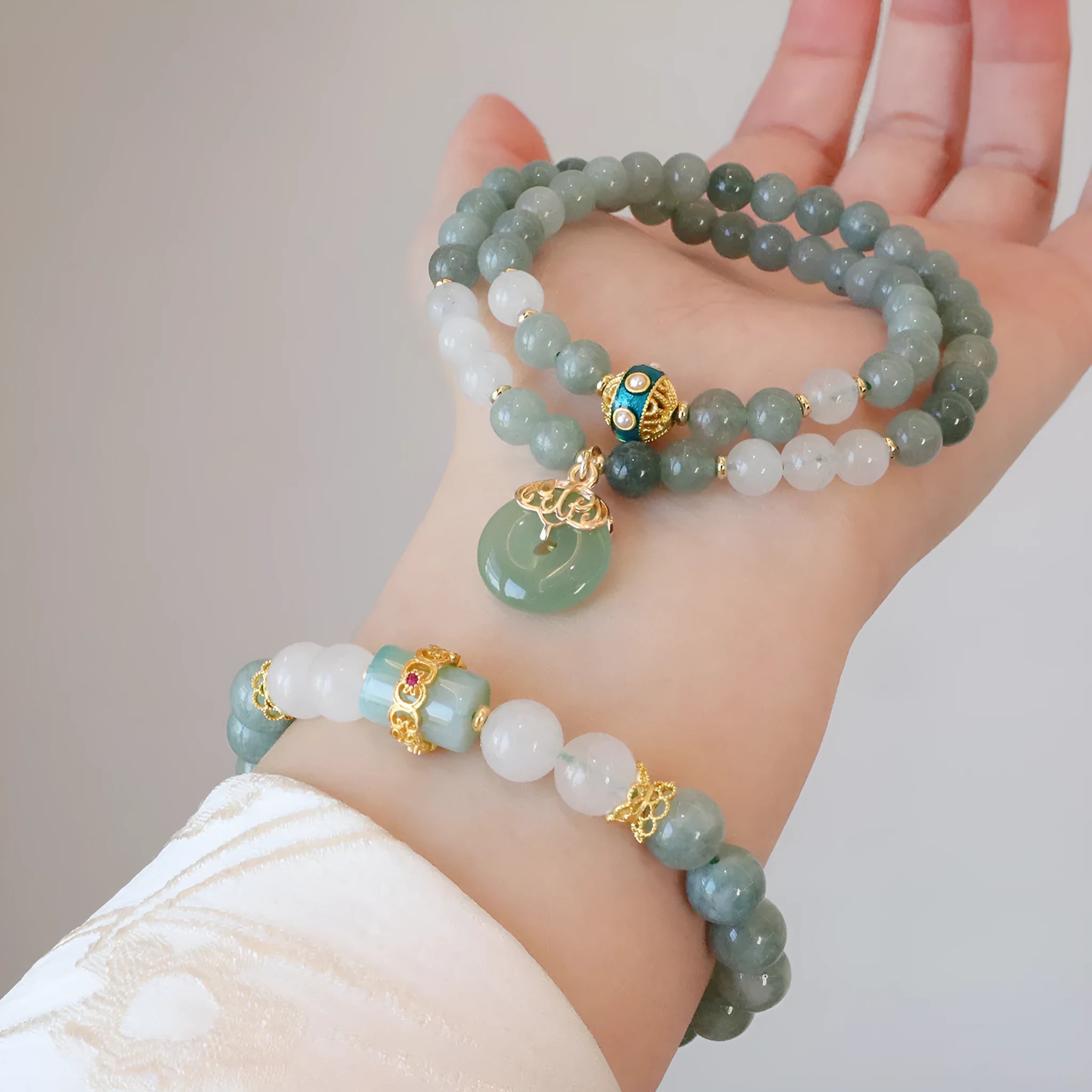 Close-up of a women's Myanmar jade bracelet with a silver geometric safety buckle pendant and lucky bead charms.