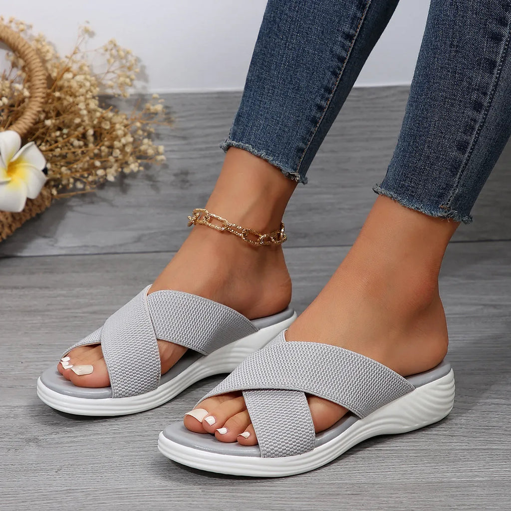 Black wedge platform slippers with a cross strap and open peep-toe design on a white background.