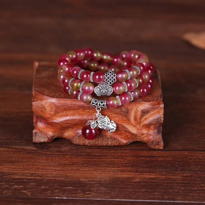 Natural watermelon crystal bracelet with a handmade Chinese knot closure, showing geometric beads.