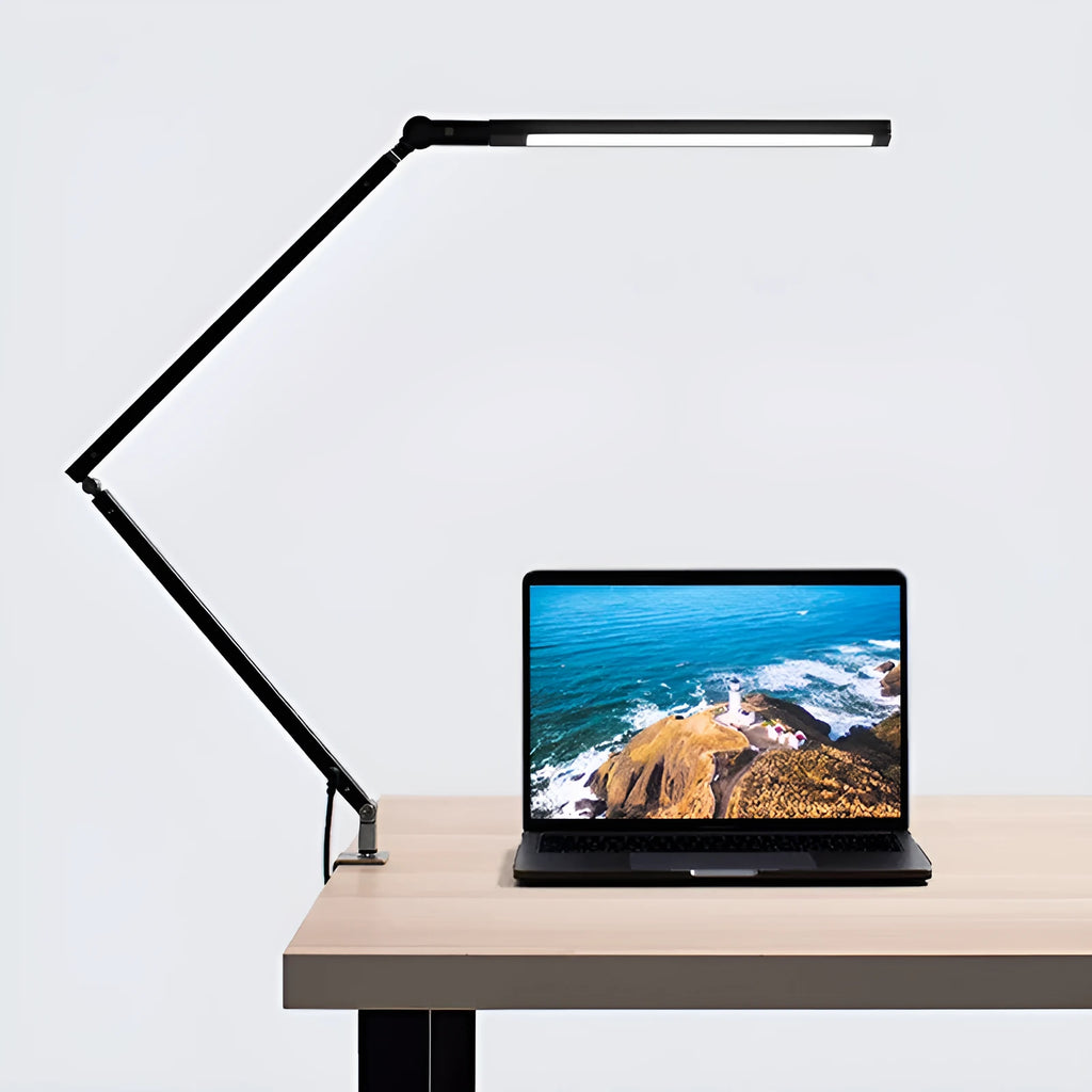 Folding aluminium desk lamp with a metal clip, shown in dazzling black, attached to a desk edge.