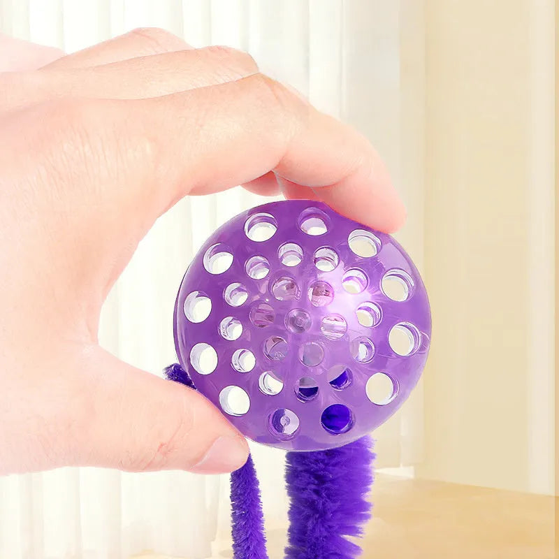 Green interactive cat toy featuring a bouncy ball with a long plush tail on a wooden floor.